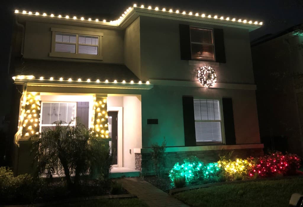 Two story install with soft white roofline lighting, a wreath accent, and color in the landscape