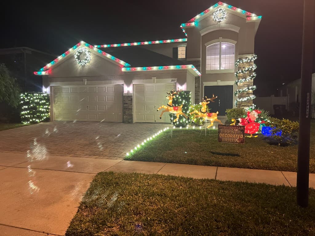 Two story home with red and green roofline lighting, vertical column wraps, and a candy cane lined driveway