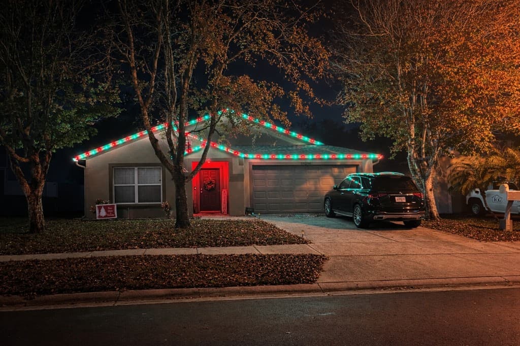 Single story home with alternating red and green roofline lighting and a red front door wreath