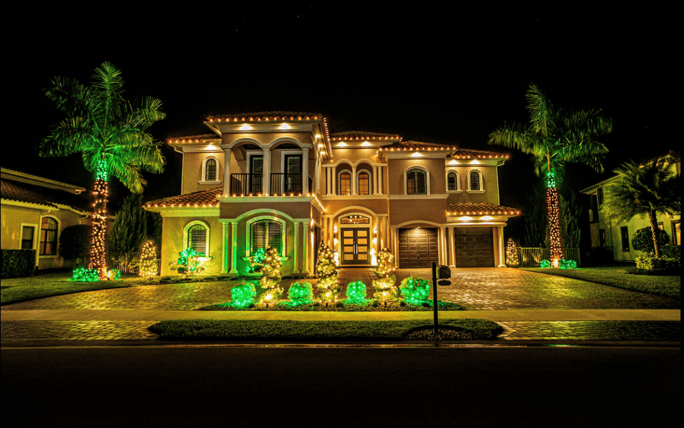 Two story Spanish style install with soft white roofline lighting plus green wrapped palms and shrubs