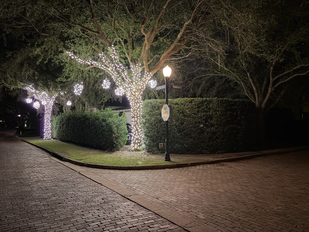 Oak trees wrapped in soft white lights with hanging light spheres at a brick-street intersection in Winter Park